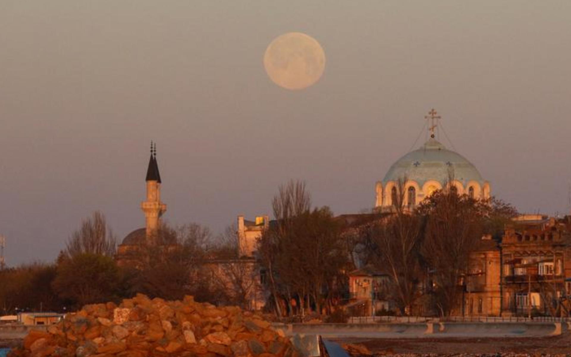 يطل القمر خلف مسجد وكاتدرائية أرثوذكسية أثناء شروق الشمس في مدينة يفباتوريا بشبه جزيرة القرم